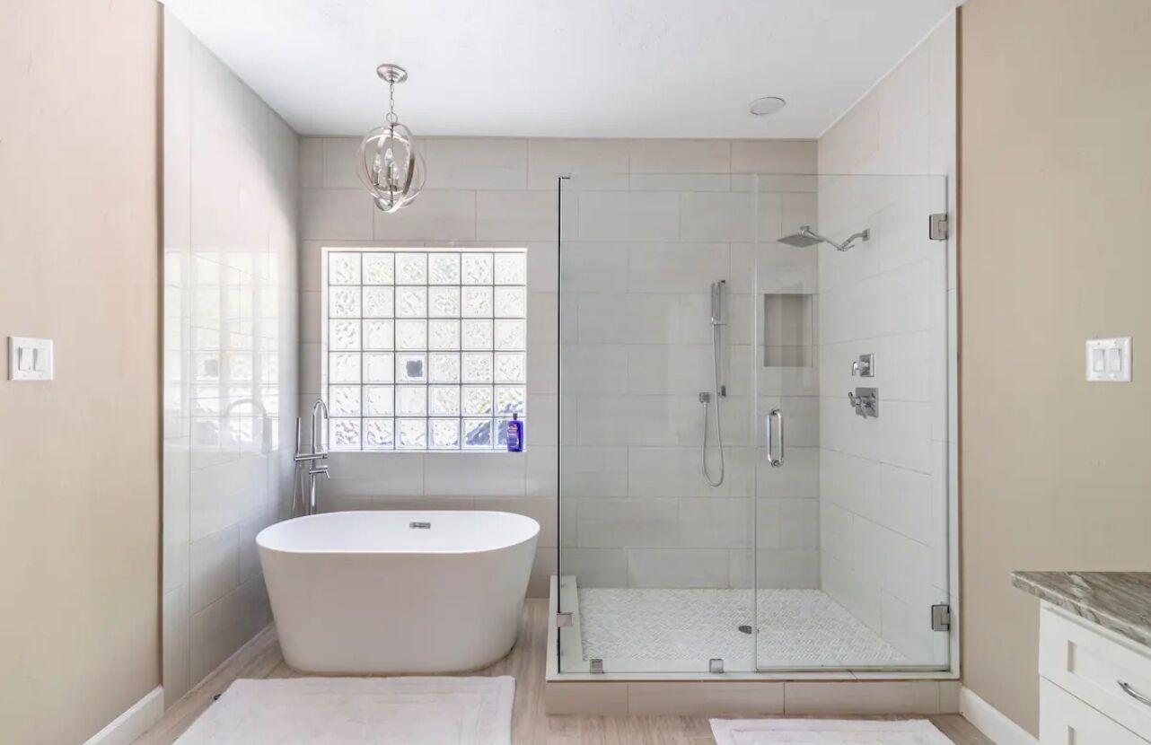 A modern bathroom with a freestanding bathtub, a glass-enclosed shower, and a window with patterned glass.