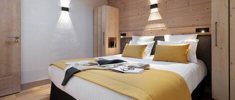 Ein modernes Schlafzimmer mit einem Holzkopfende, einem Bett mit weißer und gelber Bettwäsche sowie zwei Wandleuchten.