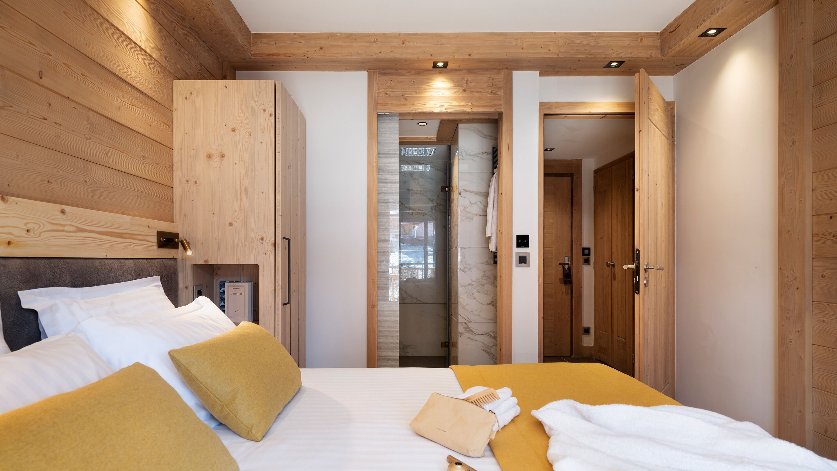 A bedroom with a bed, wooden wardrobe, and a bathroom visible through an open door.
