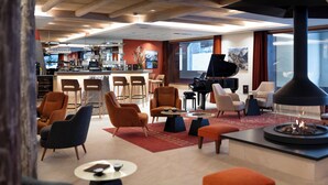 A modern hotel lobby with a bar, seating area, piano, and a fireplace. - MGM Hôtels & Résidences – Résidence Akoya (Les Avanchers-Valmorel)