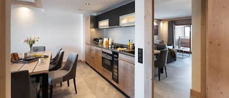 A modern kitchen with dark cabinets, a wooden dining table, and chairs. There is a breakfast setup on the table with bread, a vase of flowers, and a tray.
