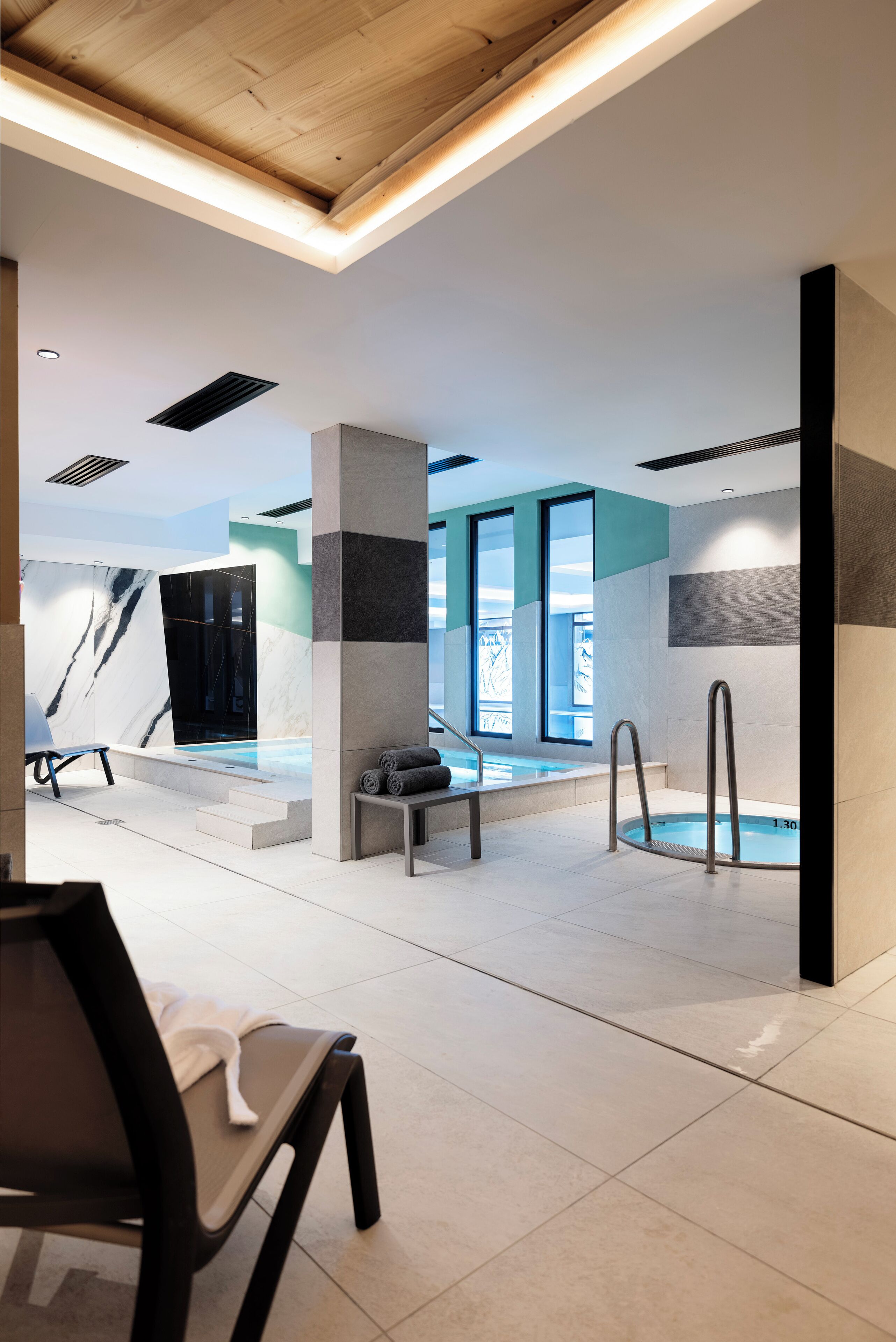 Un área interior de piscina moderna con zona de estar, un banco y una piscina con escalones de acceso.