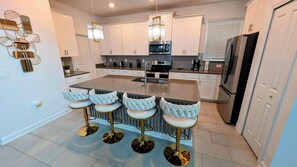 Une cuisine moderne avec des meubles blancs, un îlot central doté de tabourets, des appareils en acier inoxydable et des miroirs décoratifs sur les murs.