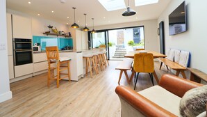 A modern kitchen with wooden cabinets, a dining area with a bench, and a living room with a sofa. - Stylish townhouse in Padstow (Padstow)