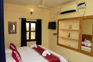 A hotel room with a bed, a television, a window with curtains, a ceiling fan, and an air conditioning unit. - Hotel Hashim By GRB (Jaisalmer)