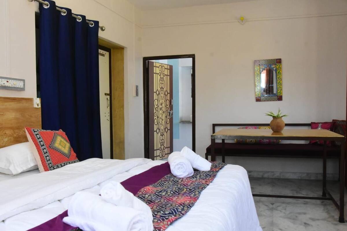 Habitación de hotel con cama, escritorio, planta en maceta y espejo en la pared.