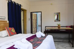 A hotel room with a bed, a desk, a potted plant, and a mirror on the wall. - Hotel Hashim By GRB (Jaisalmer)