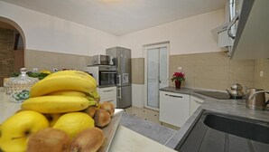 Een keuken met een fruitschaal met bananen en appels, een koelkast, een magnetron en een spoelbak.