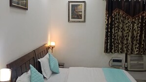 A bedroom with a bed, bedside lamps, a ceiling fan, a framed picture on the wall, and a window with curtains. - Room-home Stay Bed And Break Fast (New Delhi)