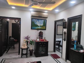 A room with a ceiling fan, an air conditioning unit, a painting, a statue, and a mirror. - Room-home Stay Bed And Break Fast (New Delhi)