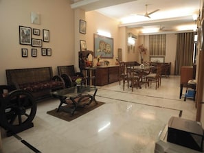 A living room with a sofa, dining table, chairs, a coffee table, and a TV. - Room-home Stay Bed And Break Fast (New Delhi)