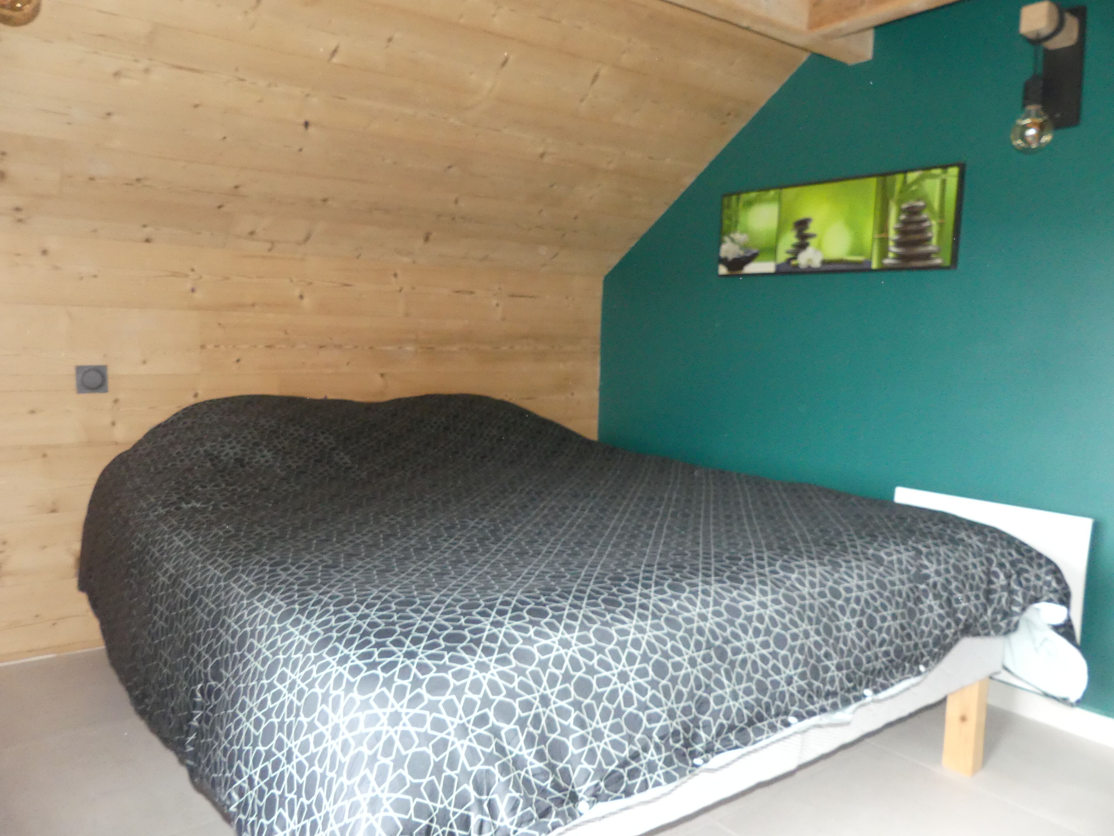 A bedroom with a bed, a wooden sloped ceiling, and a green wall with a framed picture.