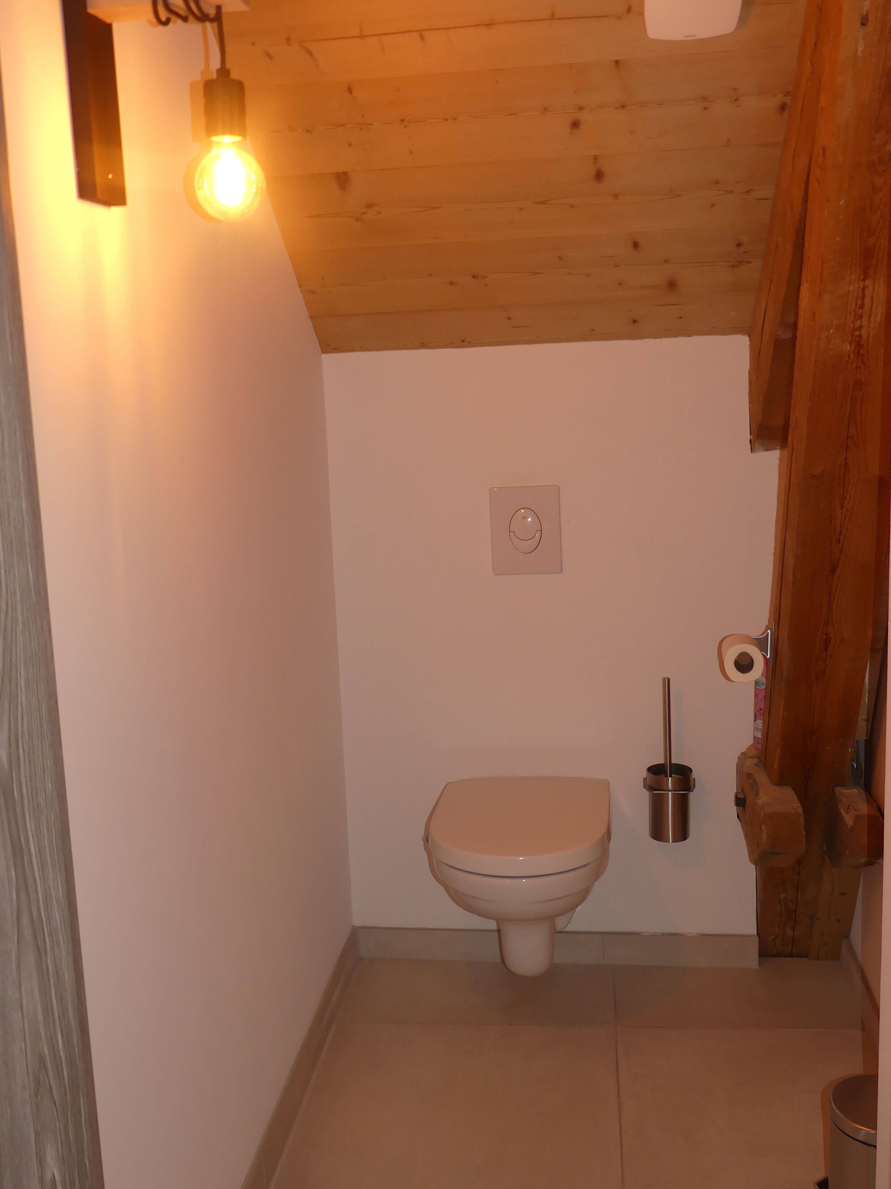 Une petite salle de bain équipée de toilettes, d’un sèche-mains et d’un luminaire au plafond.