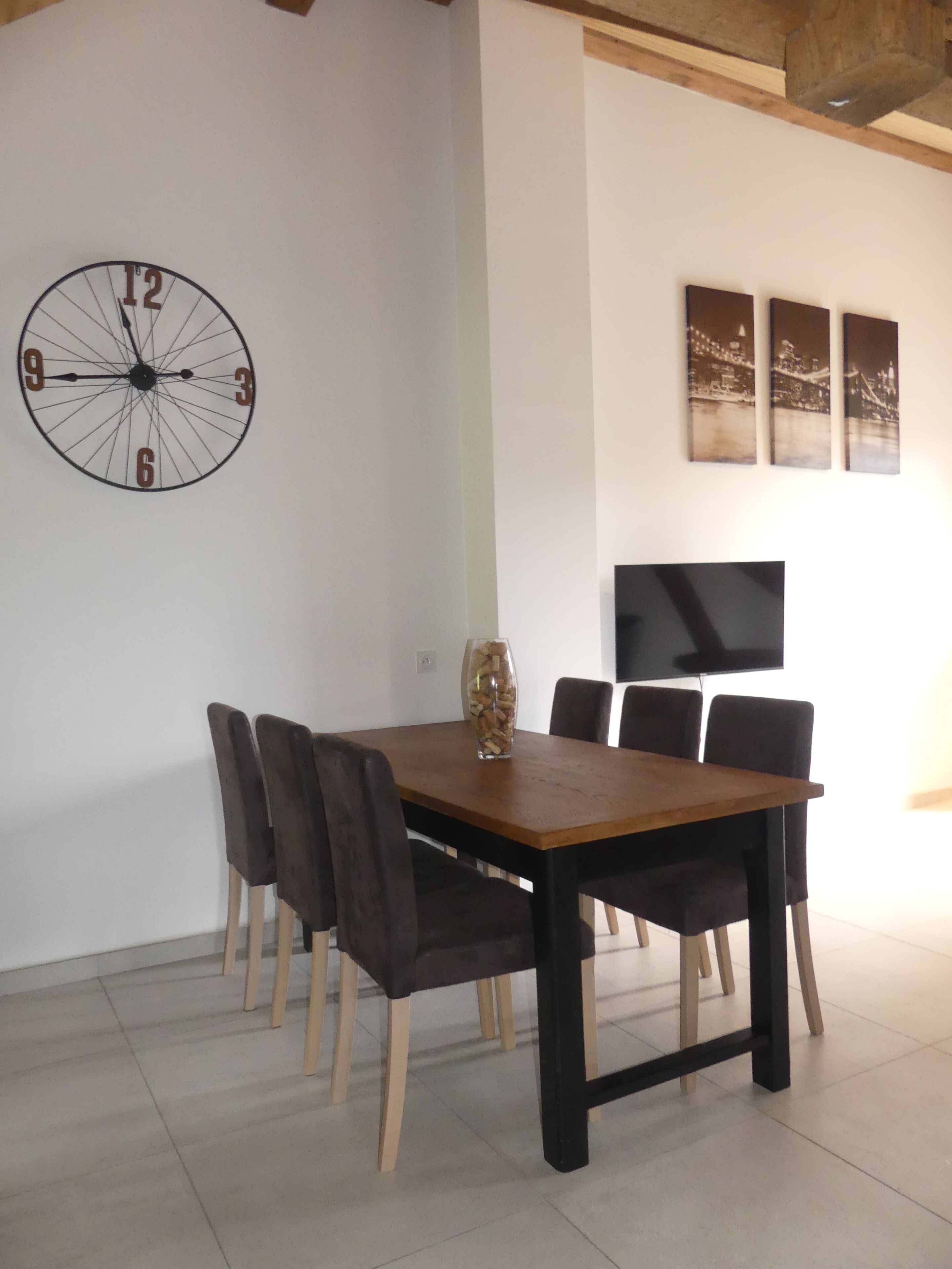 A dining area with a wooden table and chairs, a wall clock, and framed pictures.