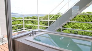 A modern bathroom with a large bathtub, a view of lush greenery, and a balcony.