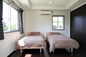 A bedroom with two beds, an air conditioning unit, a window with curtains, and a dark wardrobe. - Another Sky Ishigaki Island (Ishigaki)
