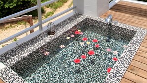A rooftop terrace with a mosaic hot tub, white railings, and a view of greenery and mountains.