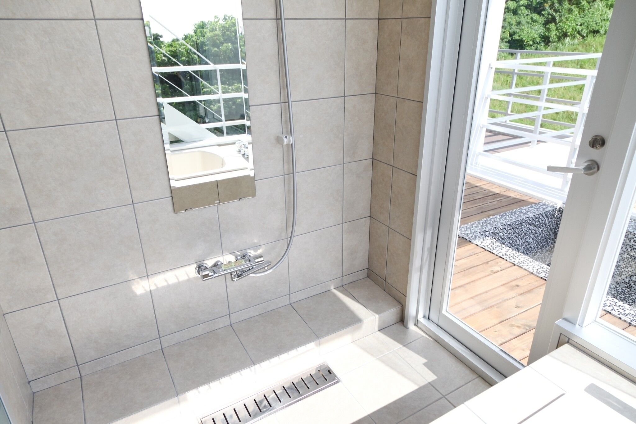 Un bagno con doccia, uno specchio e vista su un patio e vegetazione.