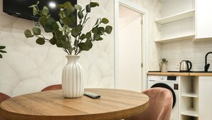 A modern kitchen with a round wooden table, a white vase with green leaves, and a washing machine. - Charming one-bedroom apartment in Madrid, close to the Tetuán metro (Madrid)