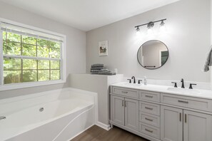 A modern bathroom with a bathtub, a vanity with a mirror, and a window providing natural light. - 5-Bed Gem Close to Duluth Fun-Sleeps 16 (Duluth)