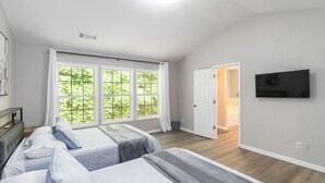 A bedroom with two beds, large windows, a TV, and a door leading to a bathroom. - 5-Bed Gem Close to Duluth Fun-Sleeps 16 (Duluth)
