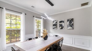A dining room with a wooden table and chairs, large windows with curtains, and abstract wall art. - 5-Bed Gem Close to Duluth Fun-Sleeps 16 (Duluth)