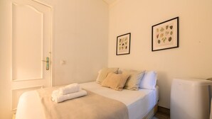 Un dormitorio con cama, almohadas, una mesita de noche, un cuadro en la pared y una puerta blanca.