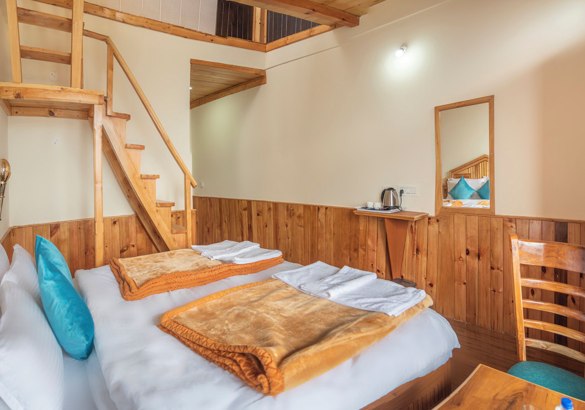A wooden-paneled room with a bed, a chair, a small table, and a staircase.