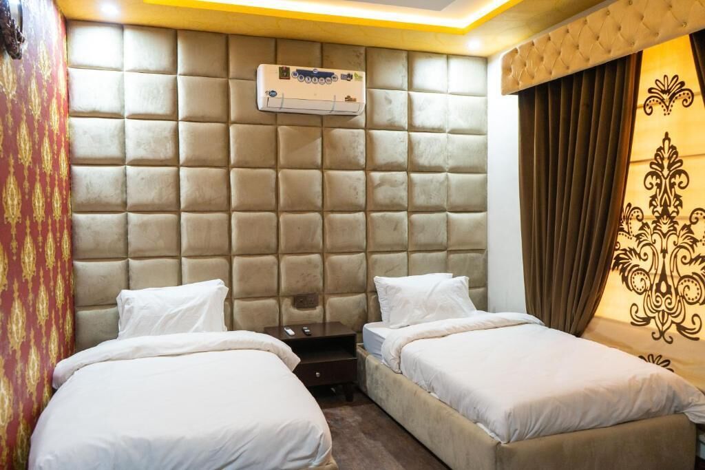 Et hotelværelse med en buet sengegavl, to enkeltsenge, et natbord og en aircondition.