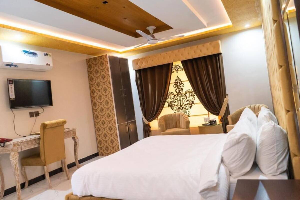 A hotel room with a bed, a desk, a chair, a television, and a ceiling fan.