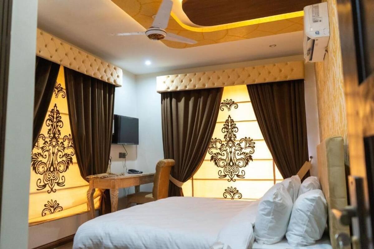 A hotel room with a bed, a desk, a chair, a ceiling fan, and decorative curtains.