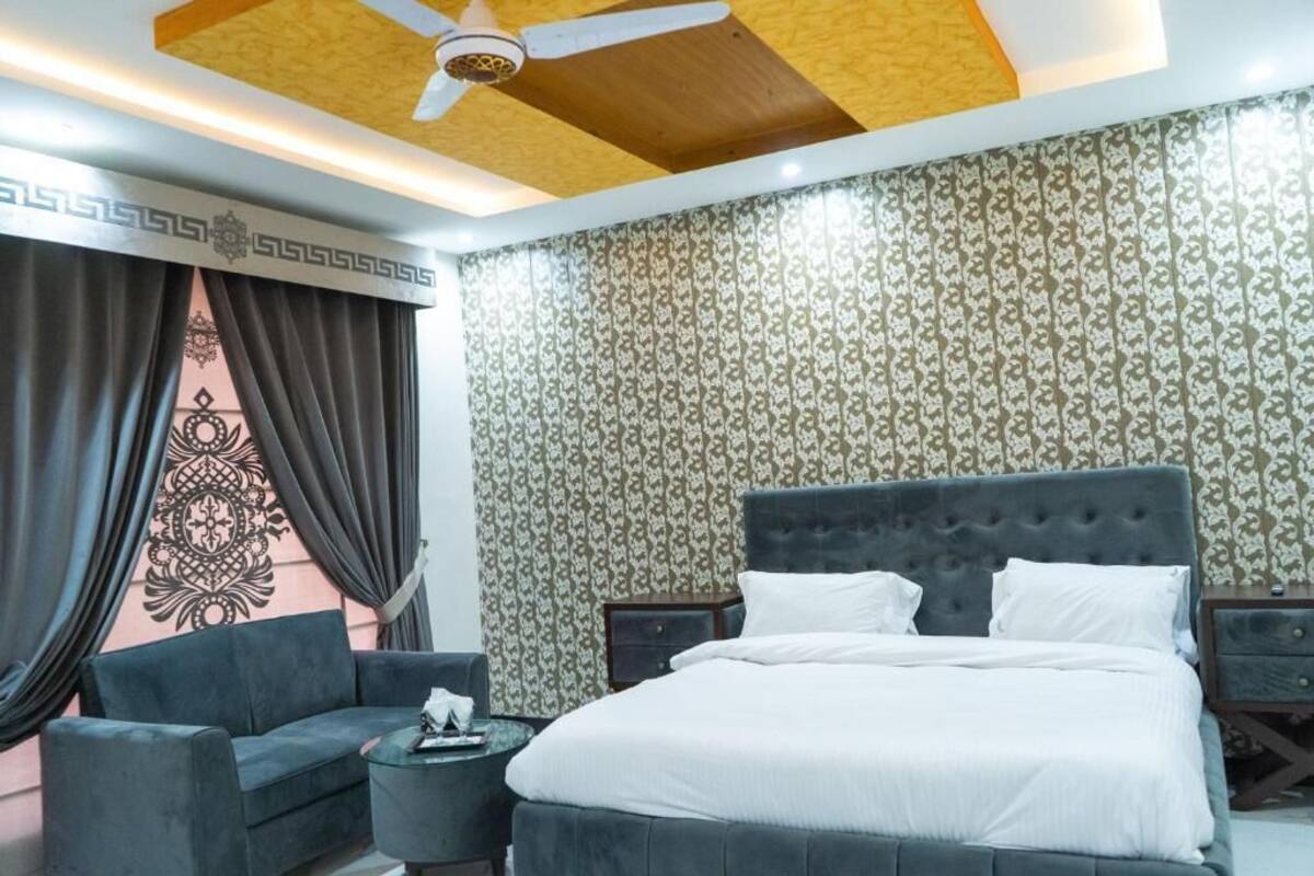 A hotel room with a large bed, a sofa, a small table, and a ceiling fan.