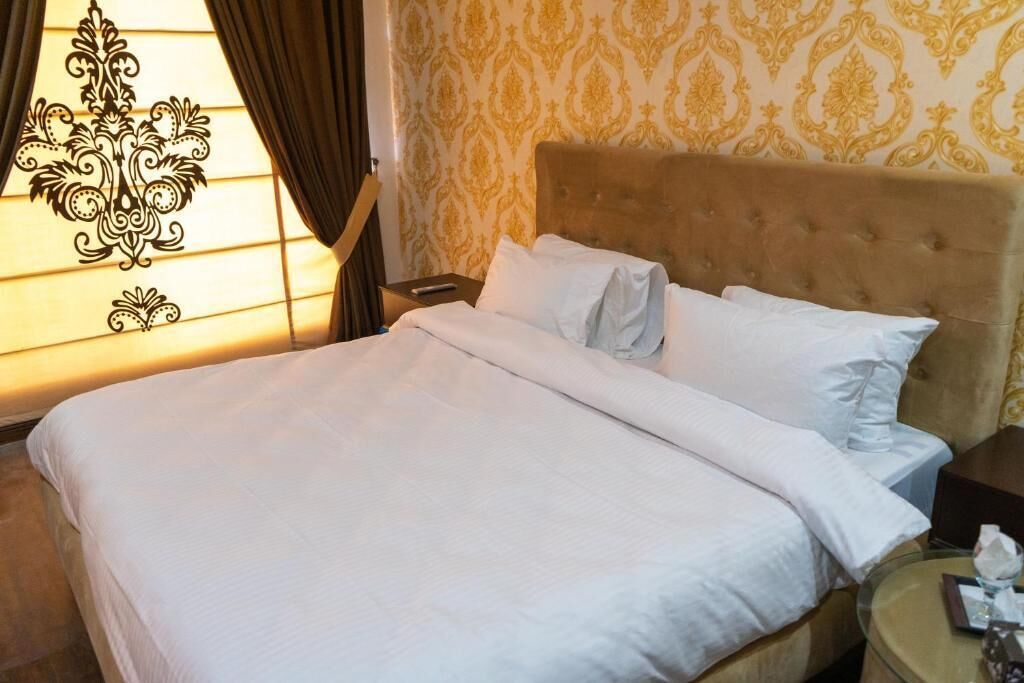Un llit ben arropat amb llençols blancs a una habitació d'hotel, amb paper tapet i un capçal tapissat.