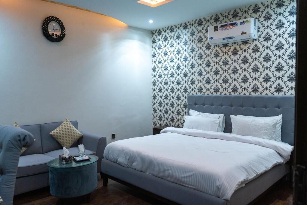 A bedroom with a grey bed, white bedding, a grey sofa, a round coffee table, and a patterned wallpaper.