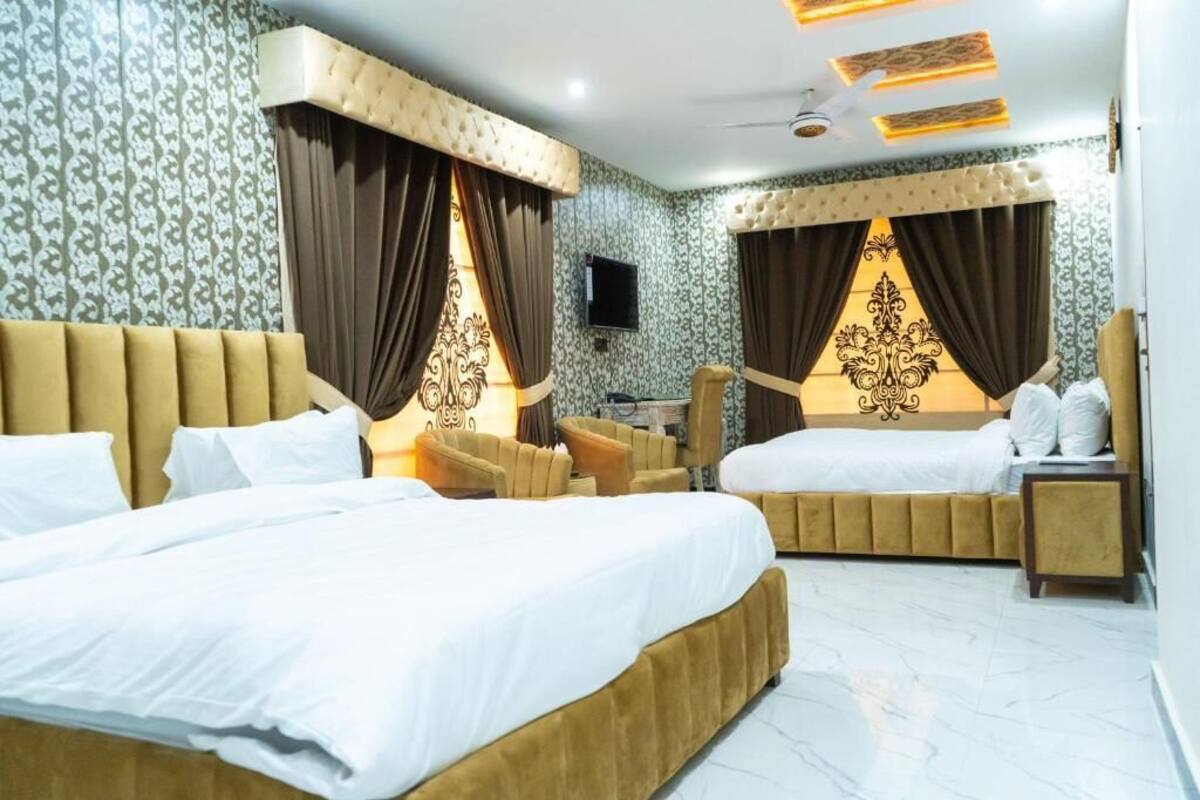 A hotel room with two beds, a sofa, a TV, and a ceiling fan.