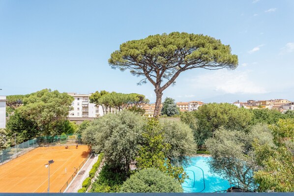 A tennis court surrounded by trees and a swimming pool.