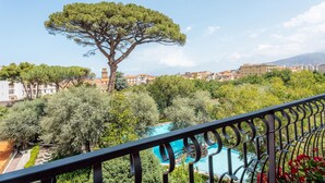 Un balcon donnant sur une piscine, entouré d’arbres et d’immeubles.