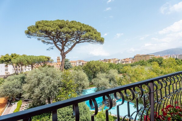A balcony with a view of a swimming pool, surrounded by trees and buildings.