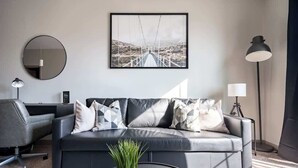 A modern living room with a grey sofa, a round mirror, a framed picture, a potted plant, and a remote control on a tray. - Luxury Downtown Apartment (Columbus)