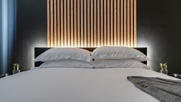 A modern bedroom with a large bed, vertical wooden slats on the wall, and two small potted plants. - Luxury Downtown Apartment (Columbus)