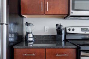 A kitchen with wooden cabinets, a blender, a knife block, and a stove. - Luxury Downtown Apartment (Columbus)