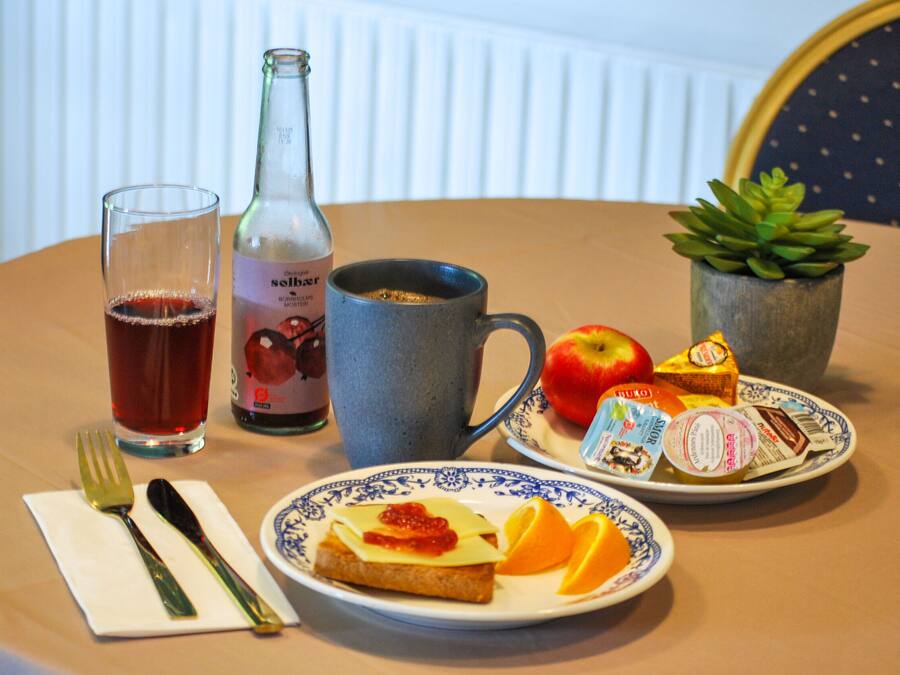 A table with a plate of toast, fruit, a glass of tea, a bottle, and a mug.