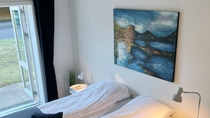 A modern bedroom with a bed, a nightstand, a lamp, and a painting on the wall. - Skovly (Viborg)