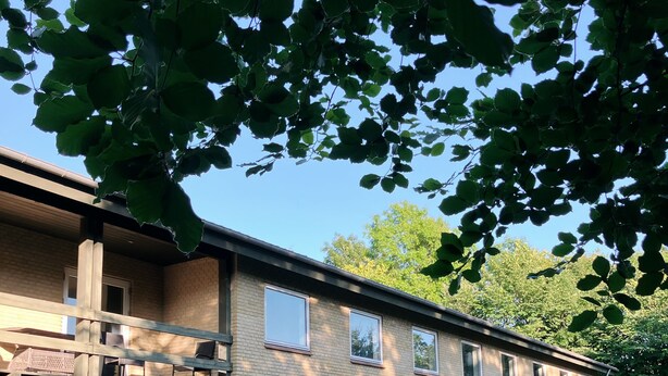 A two-story brick building with a covered patio area, outdoor seating, and a grassy lawn. - Skovly (Viborg)