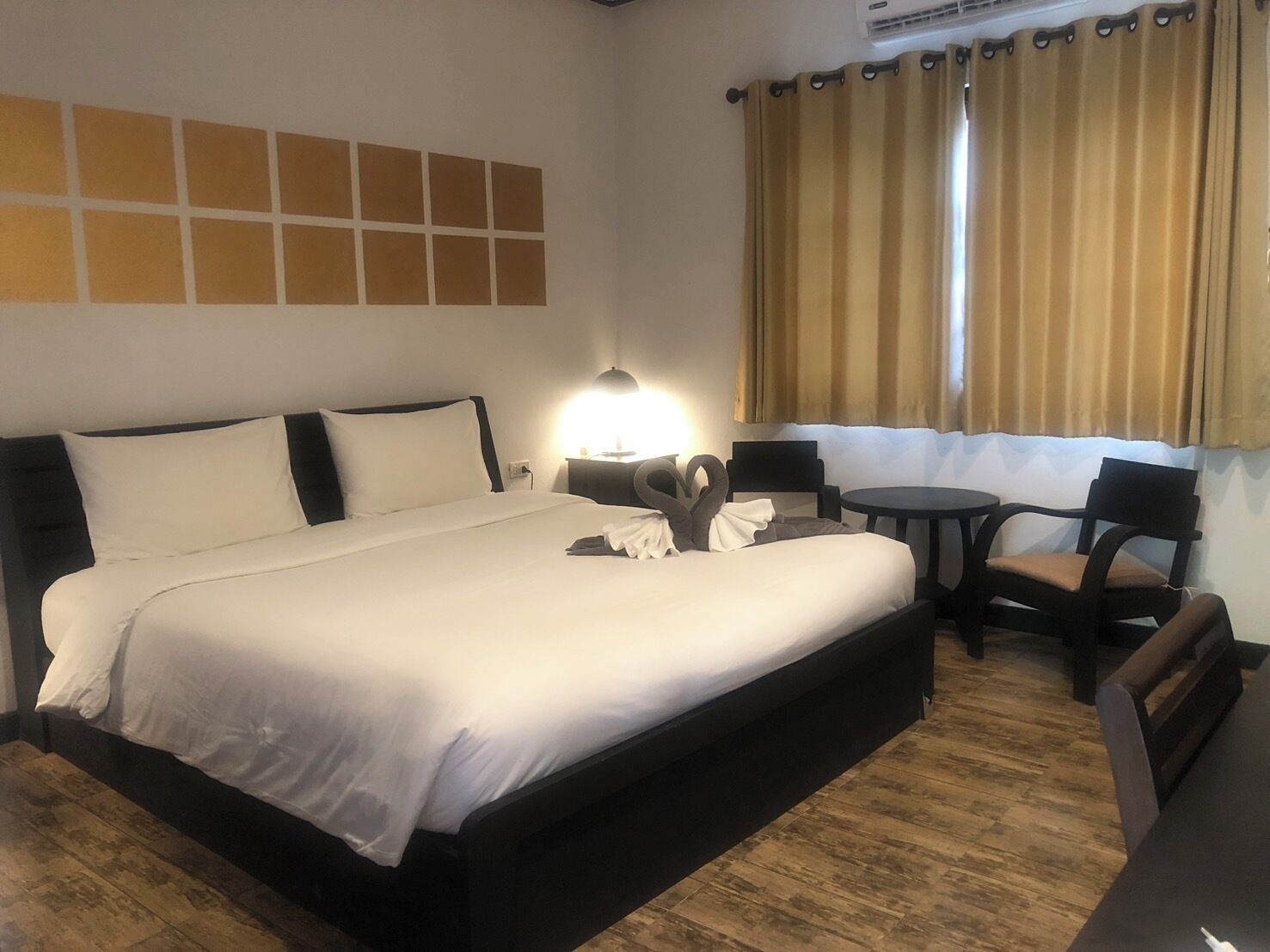A hotel room with a large bed, a desk with a chair, a lamp, and a window with curtains.