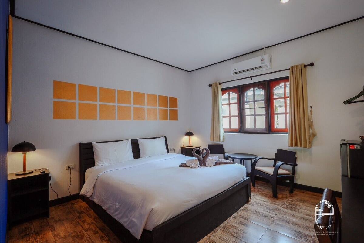 Habitación de hotel con una cama grande, un escritorio, una silla, un ventanal con cortinas y un equipo de aire acondicionado.