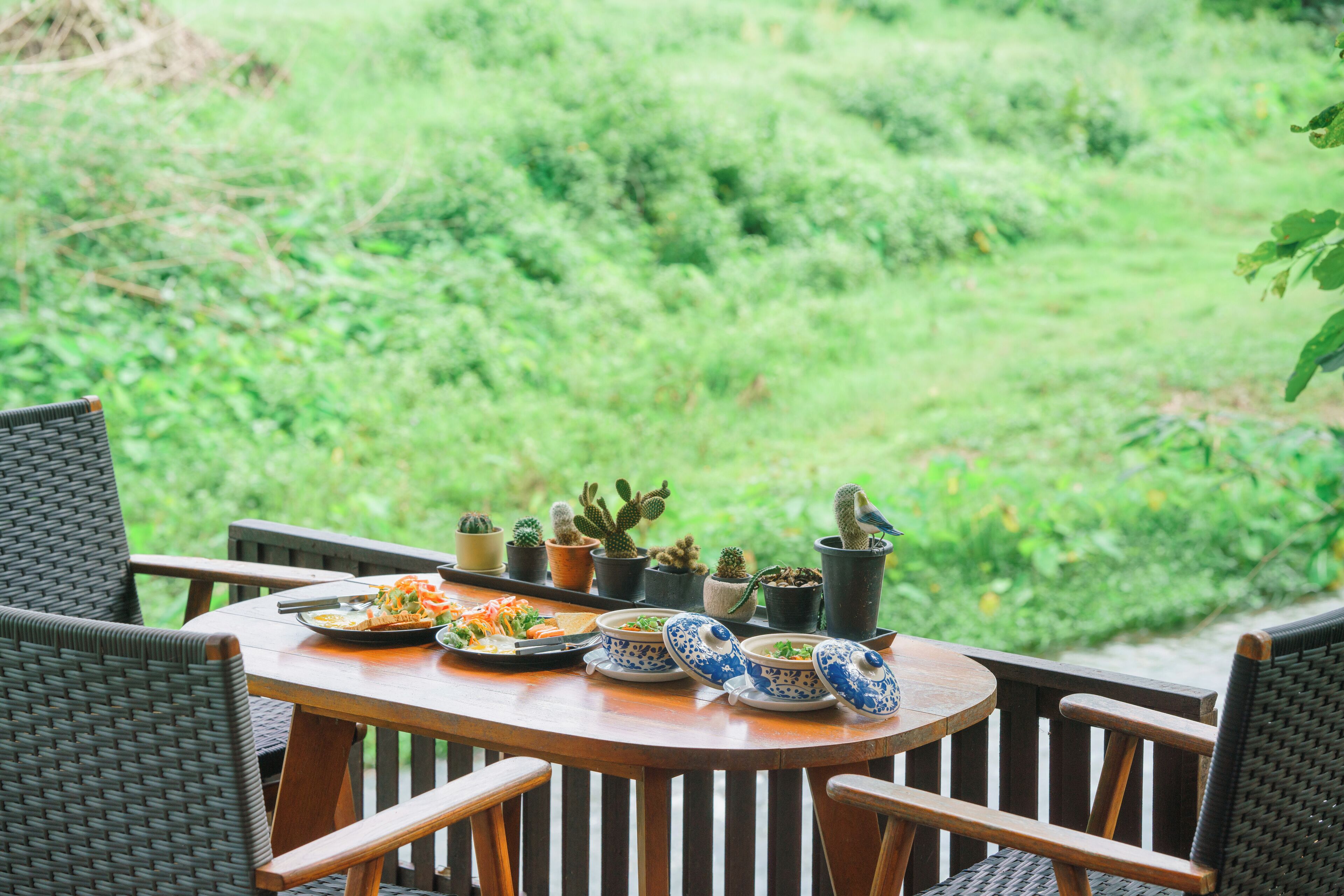 A wooden table with plates of food and blue and white patterned bowls, surrounded by wicker chairs, with potted cacti in the background.