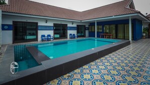A swimming pool with a tiled deck, a covered patio area, and a building with numbered doors. - Pastela Doi Saket Villa & Spa (Doi Saket)