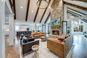 A spacious living area with a stone fireplace, leather sofas, and a large window overlooking a forest.