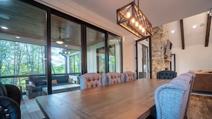 A modern dining area with a long wooden table, cushioned chairs, and a stone accent wall. - Comfy Bear Mountain Lodge| Family-Friendly (Helen)